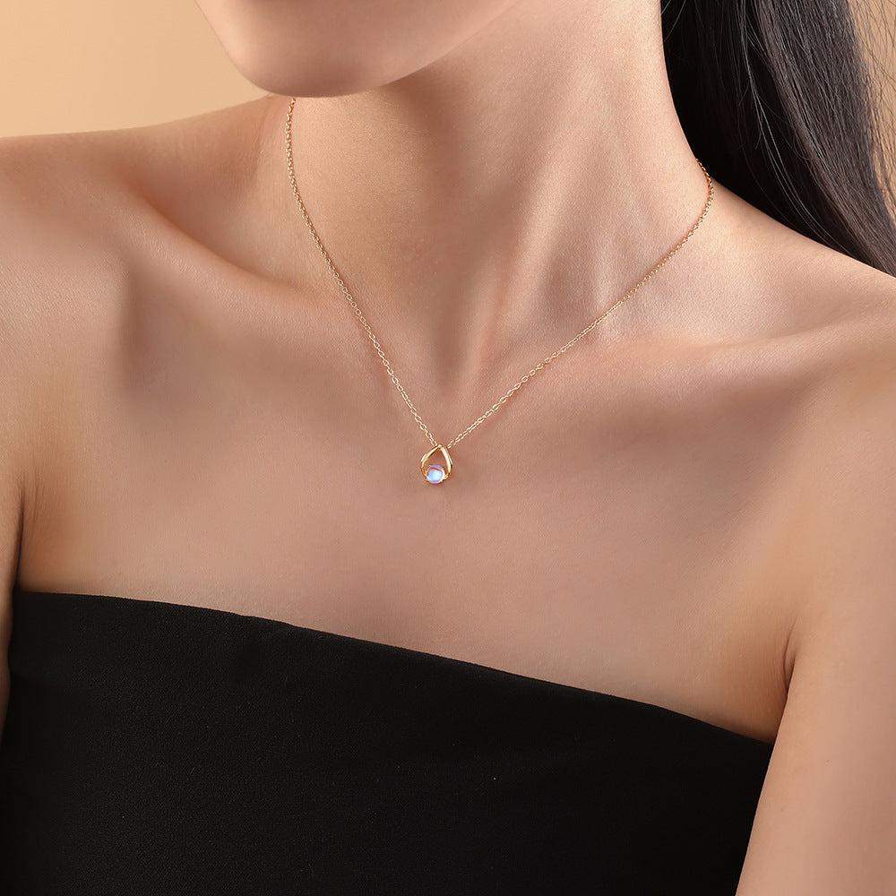 Collier Grace Lunaire en argent plaqué or, orné d'une pierre de lune bleutée aux reflets irisés, suspendue à une chaîne fine. Le pendentif, en forme de goutte stylisée, est mis en valeur sur le décolleté d'une femme.