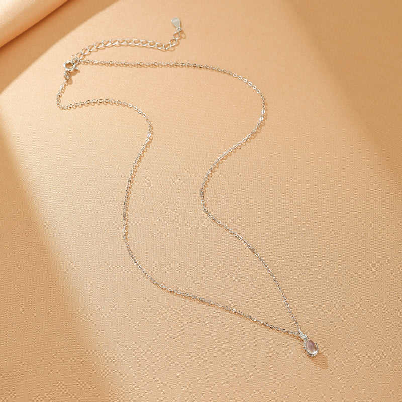 Collier fin en argent plaqué or avec un pendentif en forme de gouttelette de pierre de lune translucide, sur fond texturé beige.