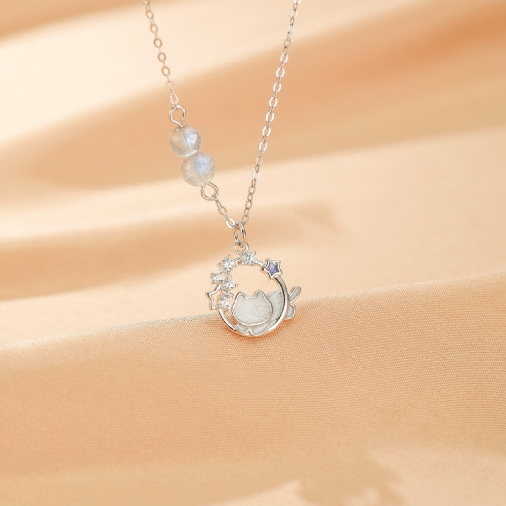 Gros plan sur le pendentif du collier Rêve Lunaire : un chaton endormi sur une lune stylisée, entouré d'étoiles, avec une pierre de lune.