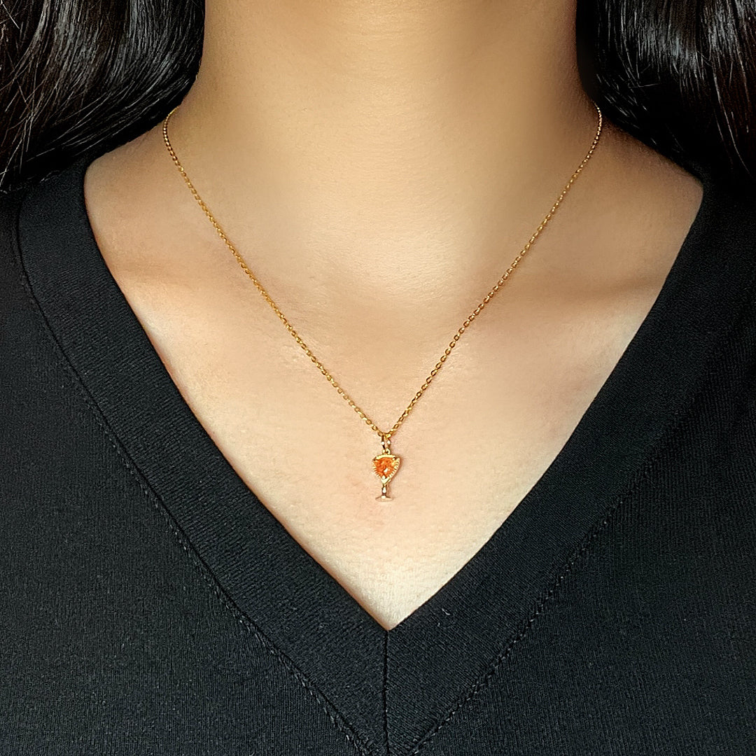 Collier plaqué or avec un pendentif en forme de calice serti d'une pierre de soleil orange, porté sur un décolleté noir.