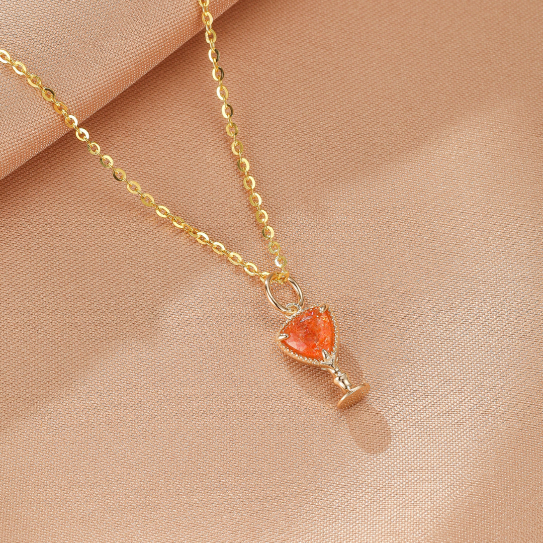 Collier plaqué or avec une pierre de soleil orange en forme de calice, sur fond rose.