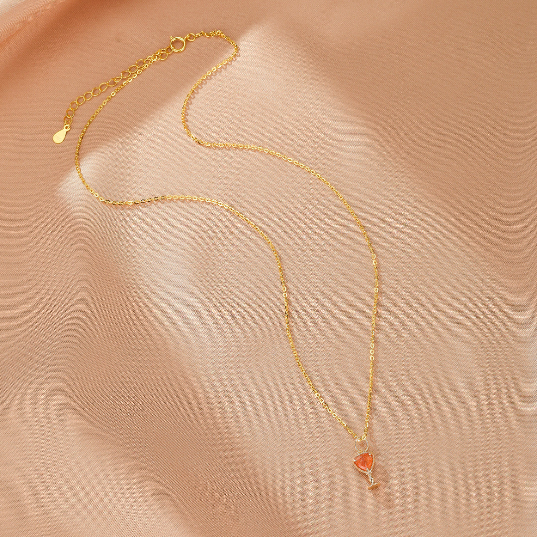 Collier délicat en argent plaqué or avec un pendentif en forme de calice rempli d'une pierre orange rappelant le soleil, sur un fond satiné rose pâle.