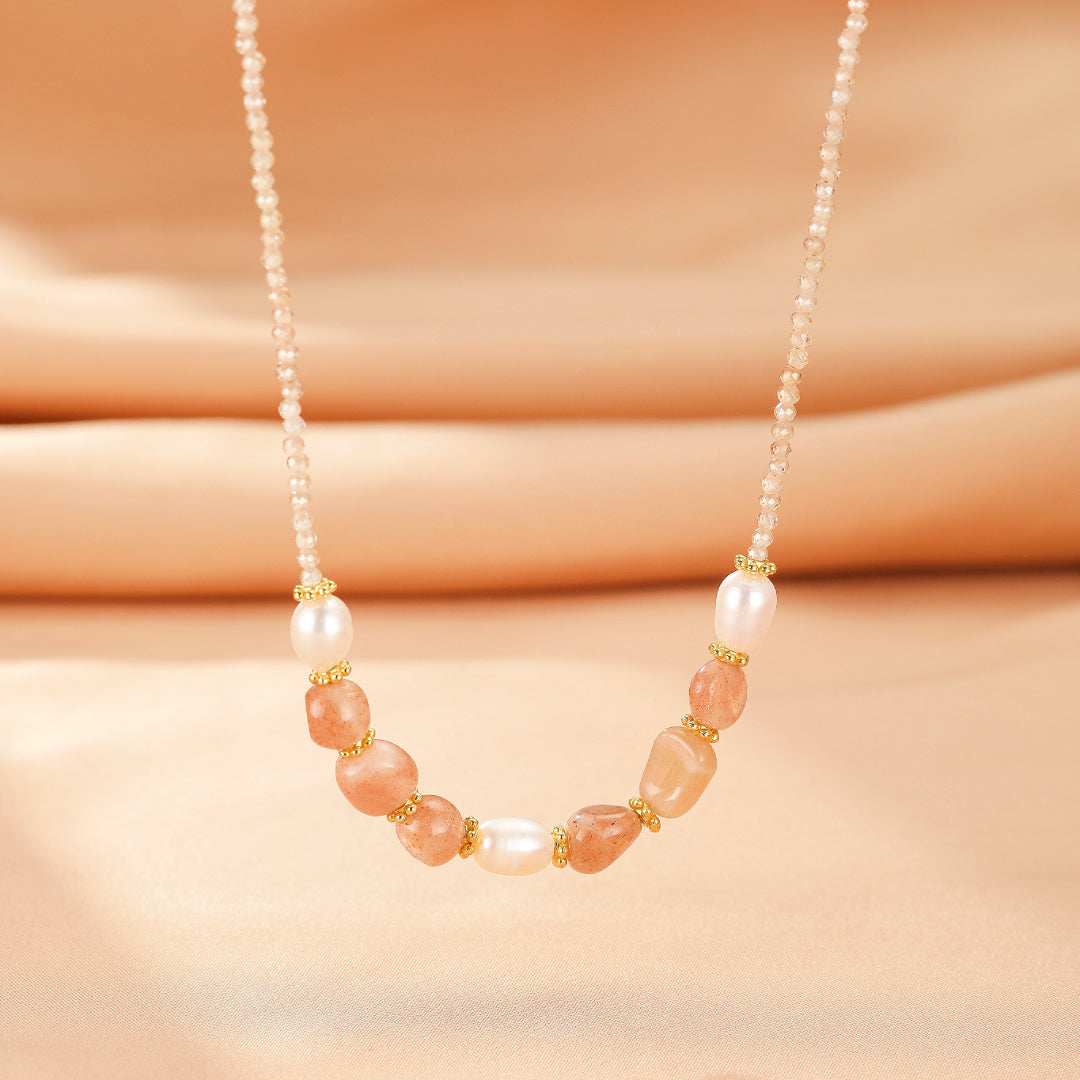 Collier "Harmonie Radieuse" avec pierres de soleil irrégulières, perles nacrées et petites perles dorées, sur une chaîne délicate aux tons rosés sur fond satiné.