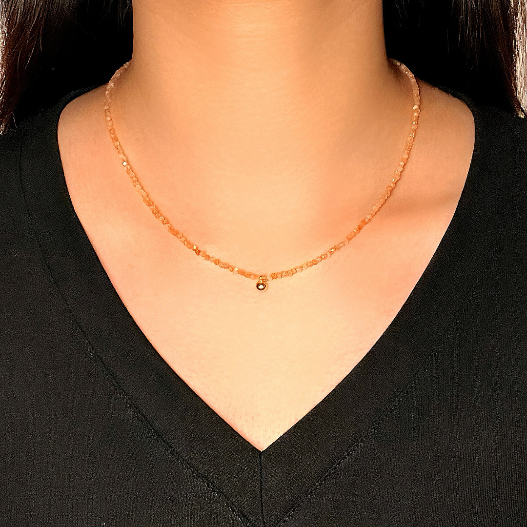 Collier délicat en pierre de soleil orange avec une petite breloque dorée, porté par une femme sur un t-shirt noir.