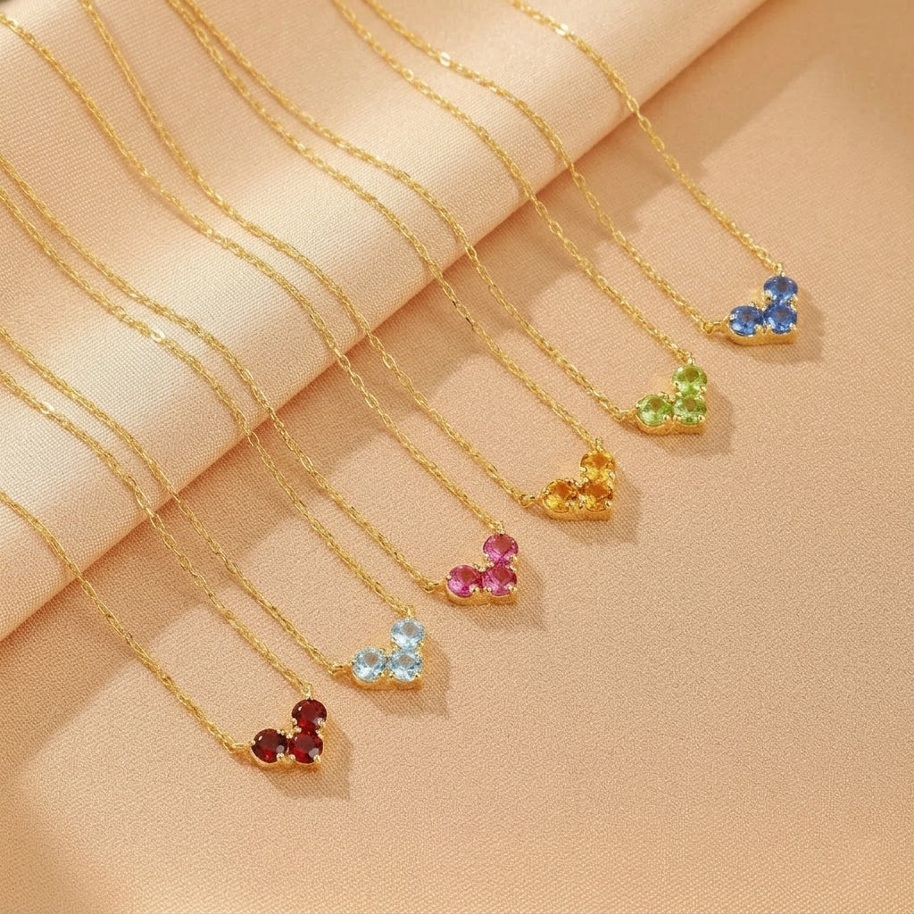 Plusieurs colliers en argent plaqué or, chacun orné d'un cœur composé de pierres de naissance colorées : rouge, bleu clair, rose, jaune, vert et bleu.