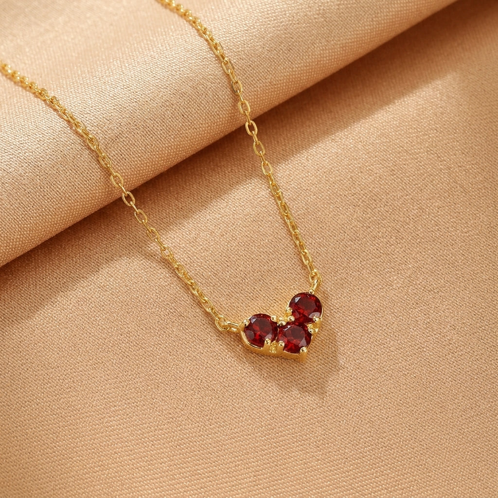 Collier en argent plaqué or avec trois pierres rouges rondes disposées en forme de cœur.