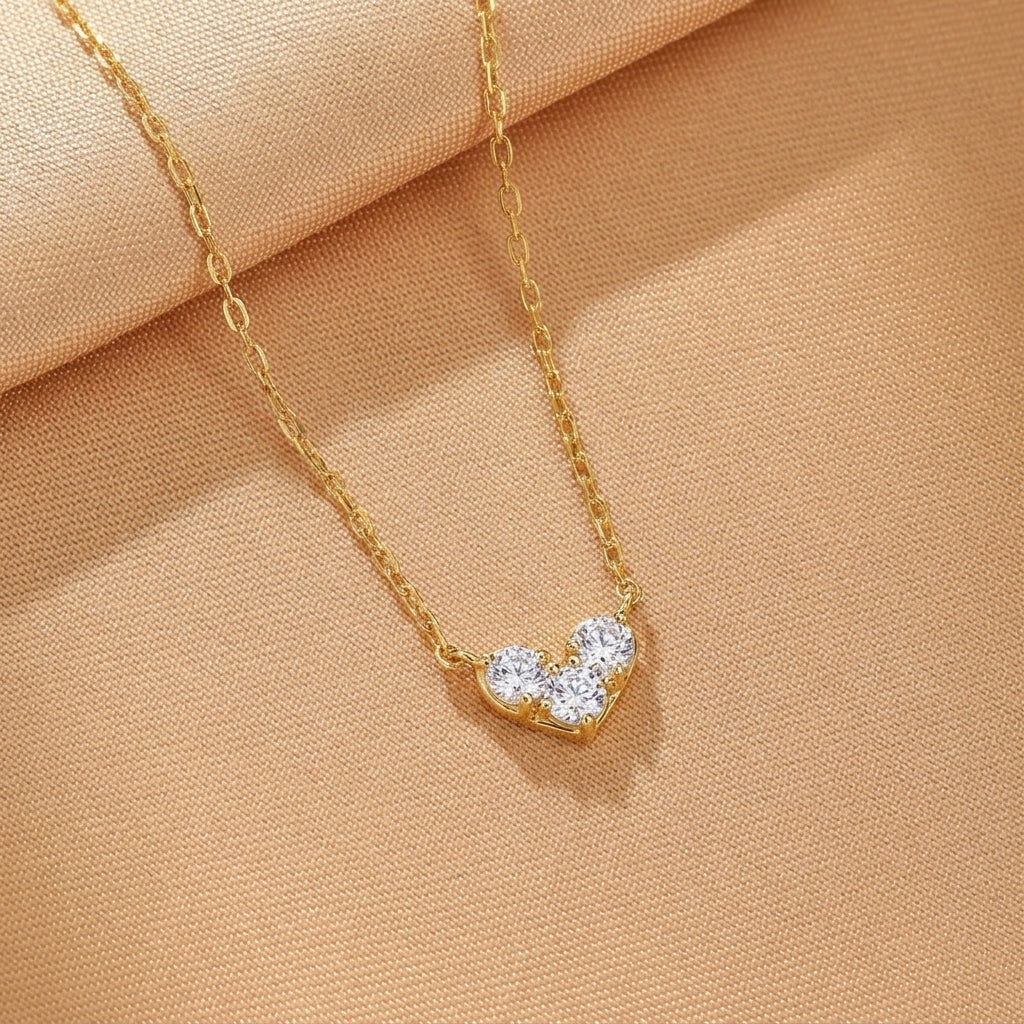 Collier en argent plaqué or avec un pendentif en forme de cœur composé de trois pierres blanches scintillantes.