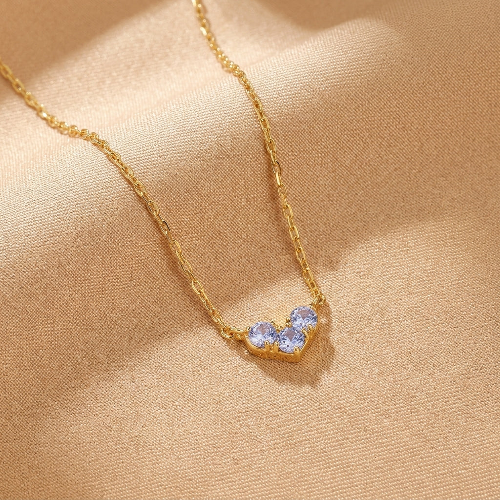 Collier en argent plaqué or avec un pendentif en forme de cœur composé de trois petites pierres bleues scintillantes.