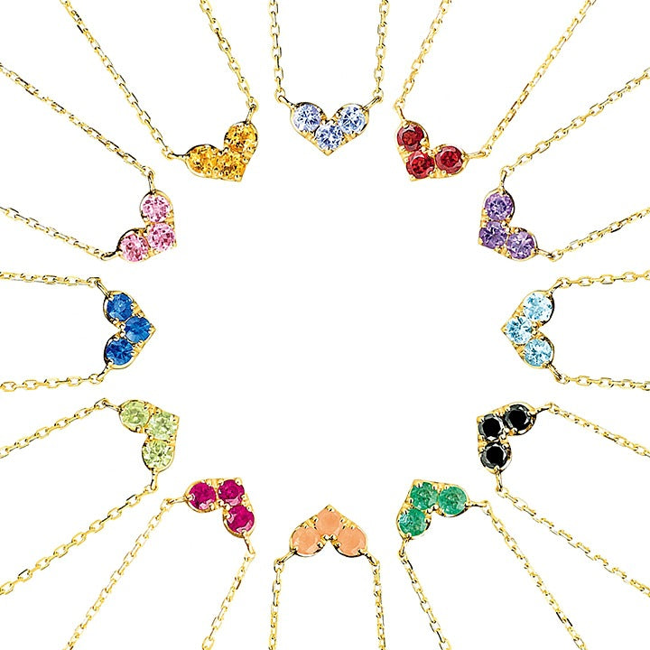 Collection de colliers en forme de cœur sertis de pierres de naissance colorées, montés sur une chaîne en argent plaqué or, présentés en cercle sur fond blanc.