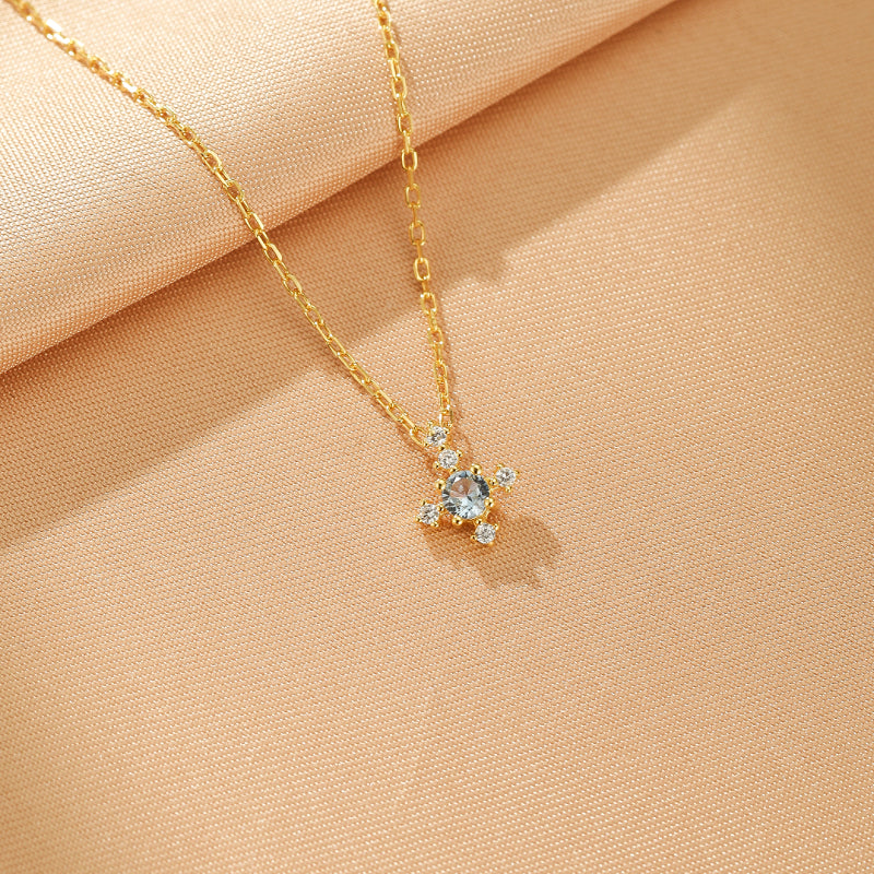 Collier en argent plaqué or avec une pierre centrale bleu clair entourée de petites pierres blanches, sur un fond texturé beige.