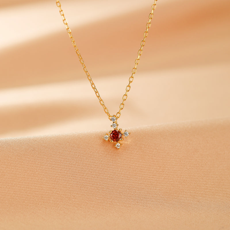 Collier en argent plaqué or avec un pendentif en forme de croix orné d'une pierre rouge centrale et de petites pierres blanches scintillantes.