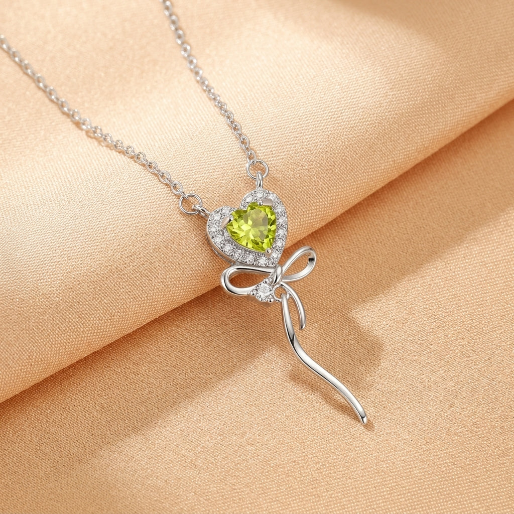Collier Cœur Enchanté en argent plaqué or 18 carats avec une pierre verte en forme de cœur entourée de petits diamants et un nœud décoratif en argent.