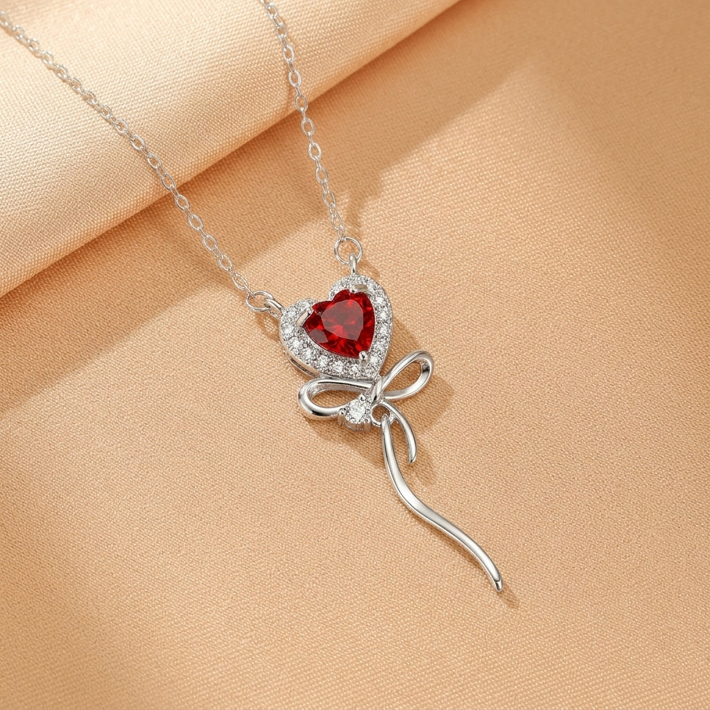 Collier en argent plaqué or 18 carats avec un pendentif en forme de cœur rouge entouré de zirconiums blancs et un nœud décoratif.