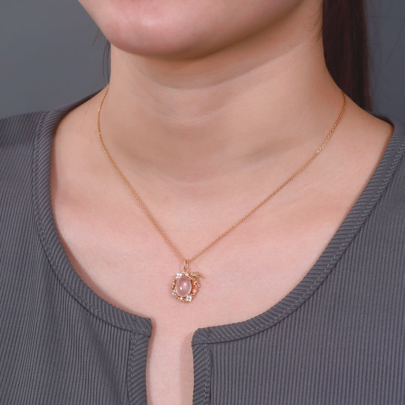 Collier en argent plaqué or avec un pendentif en quartz rose et de petits cristaux, orné d'un motif de lapin stylisé.
