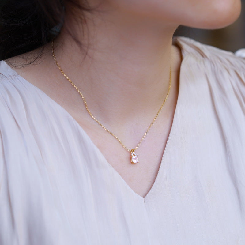 Collier fin en argent plaqué or avec un pendentif en quartz rose taillé en forme de larme, porté par une femme sur un chemisier crème.