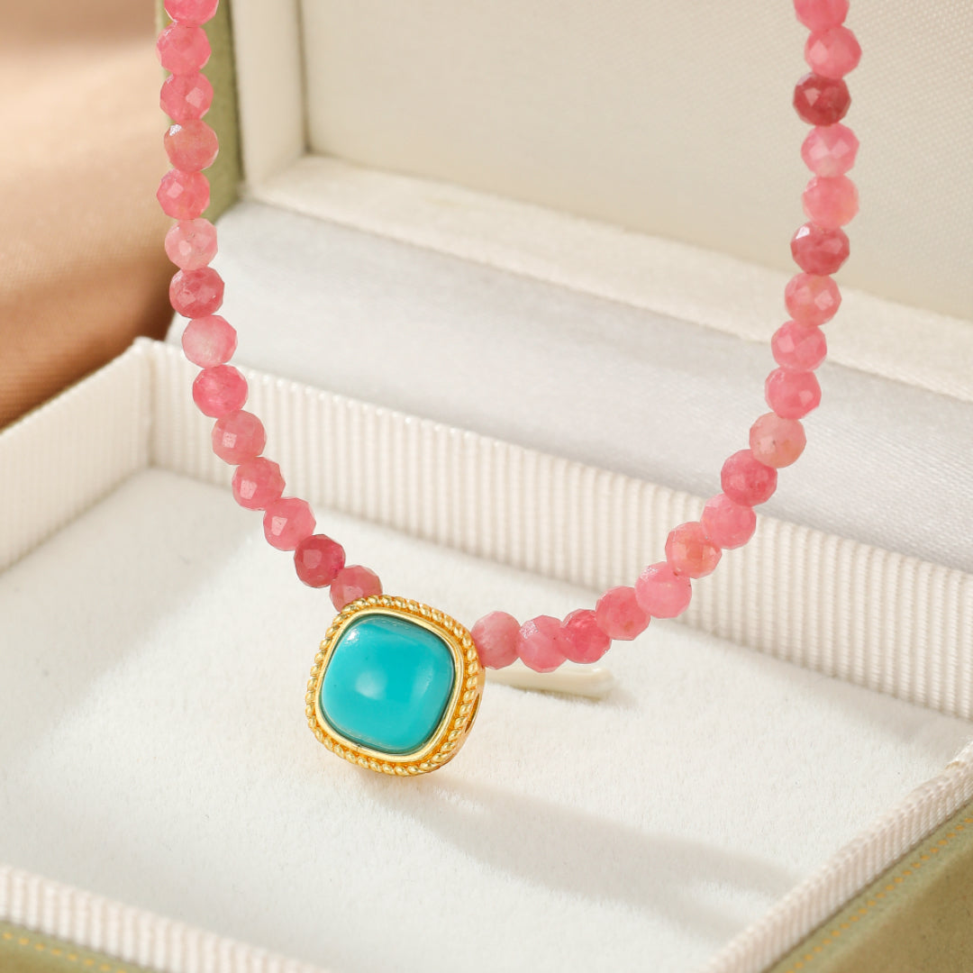 Collier élégant avec des perles roses facettées et un pendentif carré bleu turquoise serti dans un entourage doré, présenté dans une boîte cadeau.