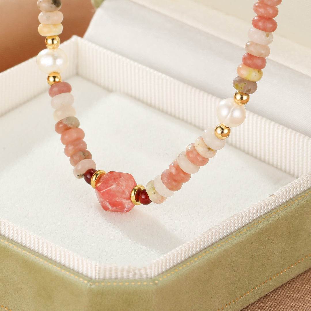 Collier artisanal avec des perles de rhodonite, de jade rose, de quartz rose, des perles d'eau douce et des accents dorés, centré sur un pendentif sculpté en forme de cristal de rhodonite.