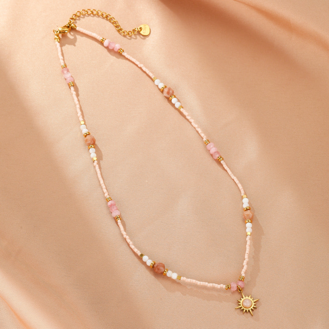 Collier fantaisie de couleur rose pâle avec des perles fines et des pierres naturelles roses et blanches, orné d'un pendentif soleil doré.