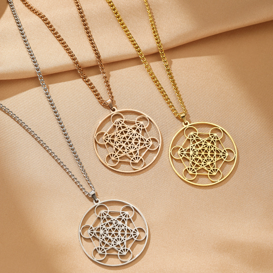 Trois colliers de géométrie sacrée Sri Yantra en or, or rose et argent, présentés sur une surface beige satinée.