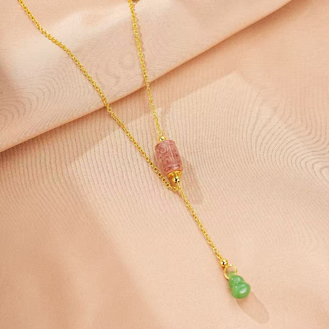 Collier doré à breloque en tourmaline rose sculptée en forme de cylindre et une petite breloque verte en forme de gourde.