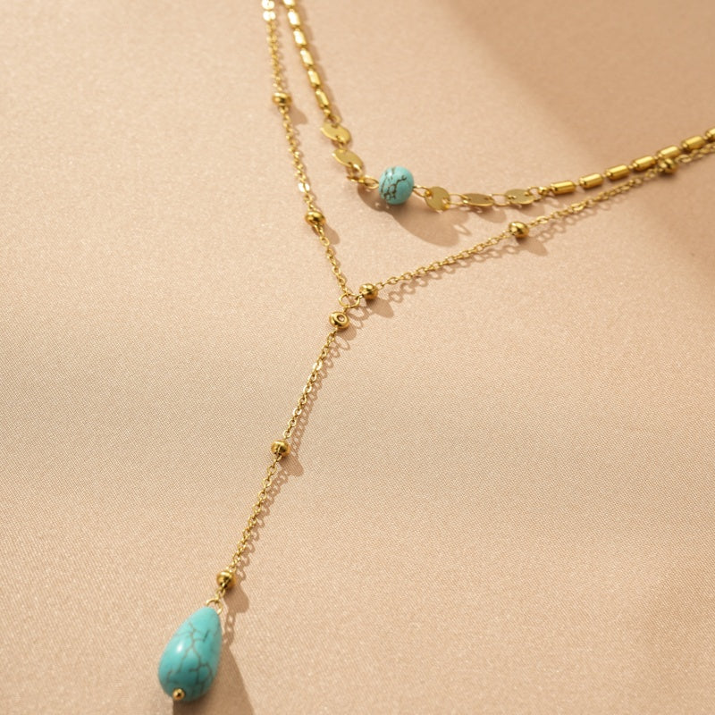 Collier double chaîne plaqué or avec une pierre turquoise en forme de goutte d'eau et une petite pierre turquoise sur la chaîne supérieure.