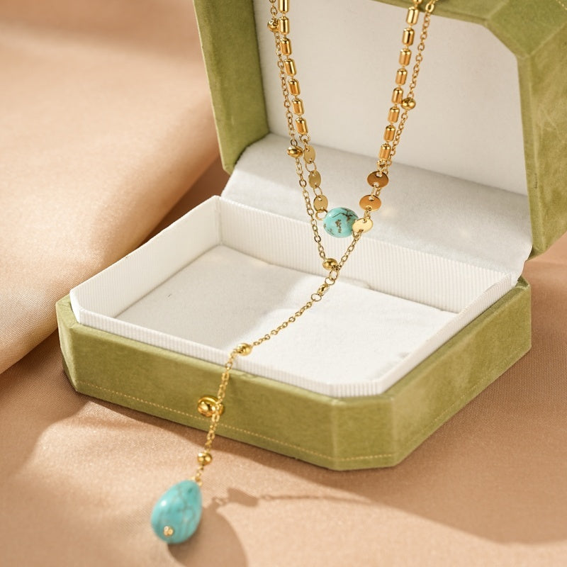 Collier plaqué or avec deux pierres de turquoise, une ovale au centre et une en forme de goutte à l'extrémité, présenté dans un écrin vert.
