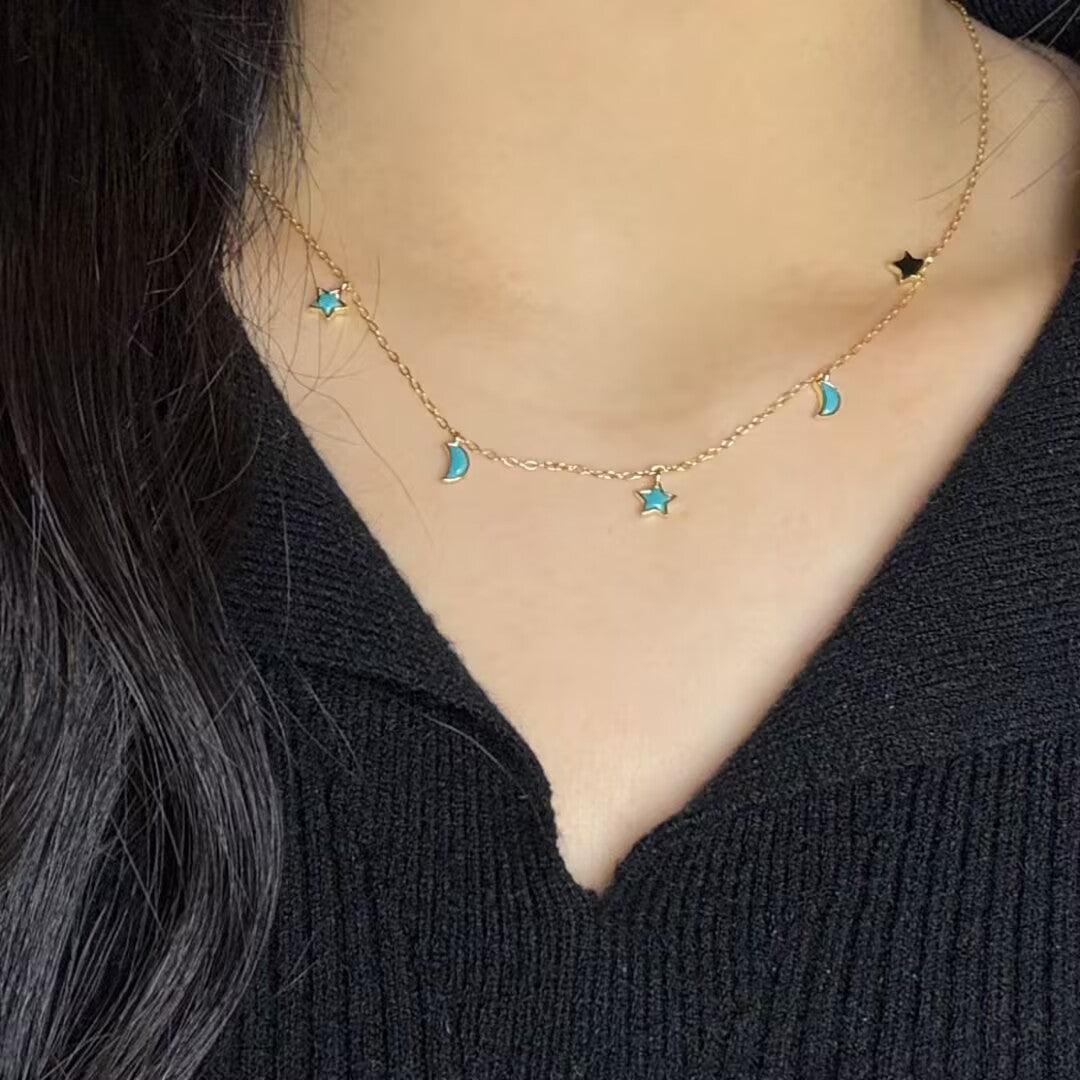 Collier plaqué or avec des breloques en forme d'étoiles et de lunes bleues turquoise sur une chaîne délicate.