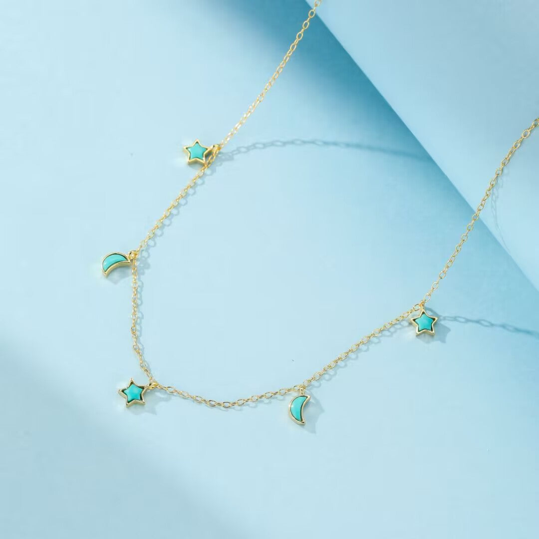 Collier en plaqué or avec des breloques en turquoise en forme d'étoile et de croissant de lune sur une chaîne délicate.