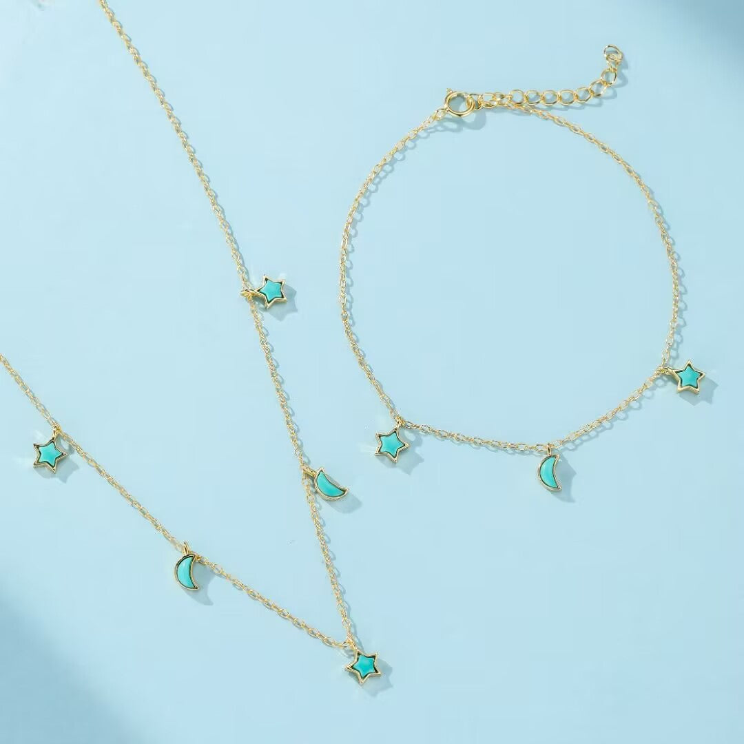 Ensemble de bijoux plaqué or avec des breloques en forme d'étoile et de croissant de lune en turquoise, sur fond bleu clair.