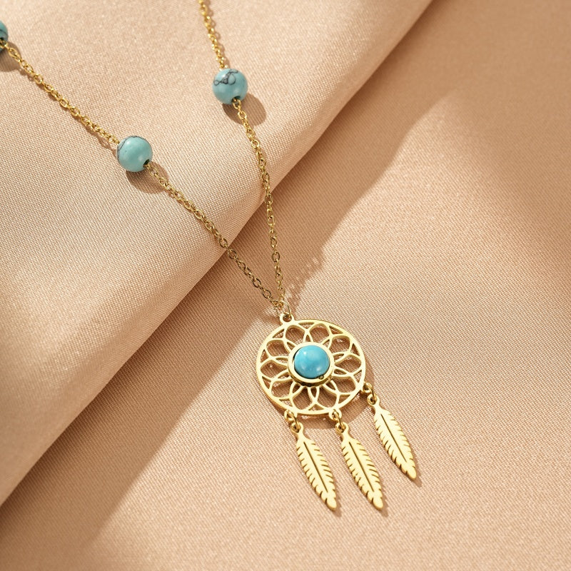 Collier avec pendentif attrape-rêves doré orné d'une turquoise centrale et de trois plumes, avec des perles turquoise sur la chaîne.