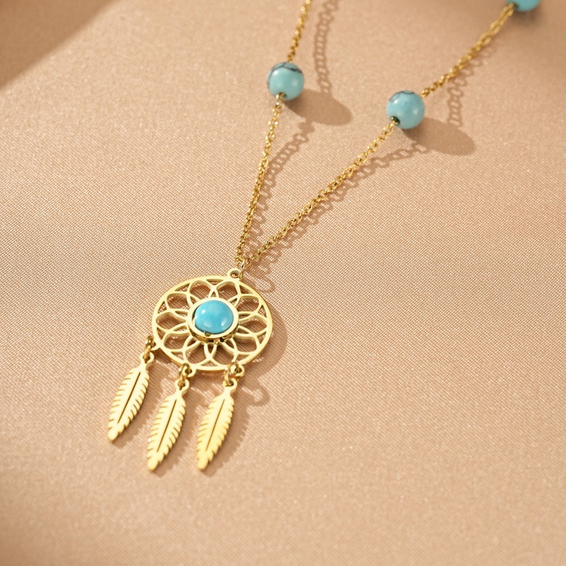 Collier plaqué or avec un pendentif attrape-rêves serti d'une turquoise et orné de trois plumes, ponctué de perles turquoise sur la chaîne.