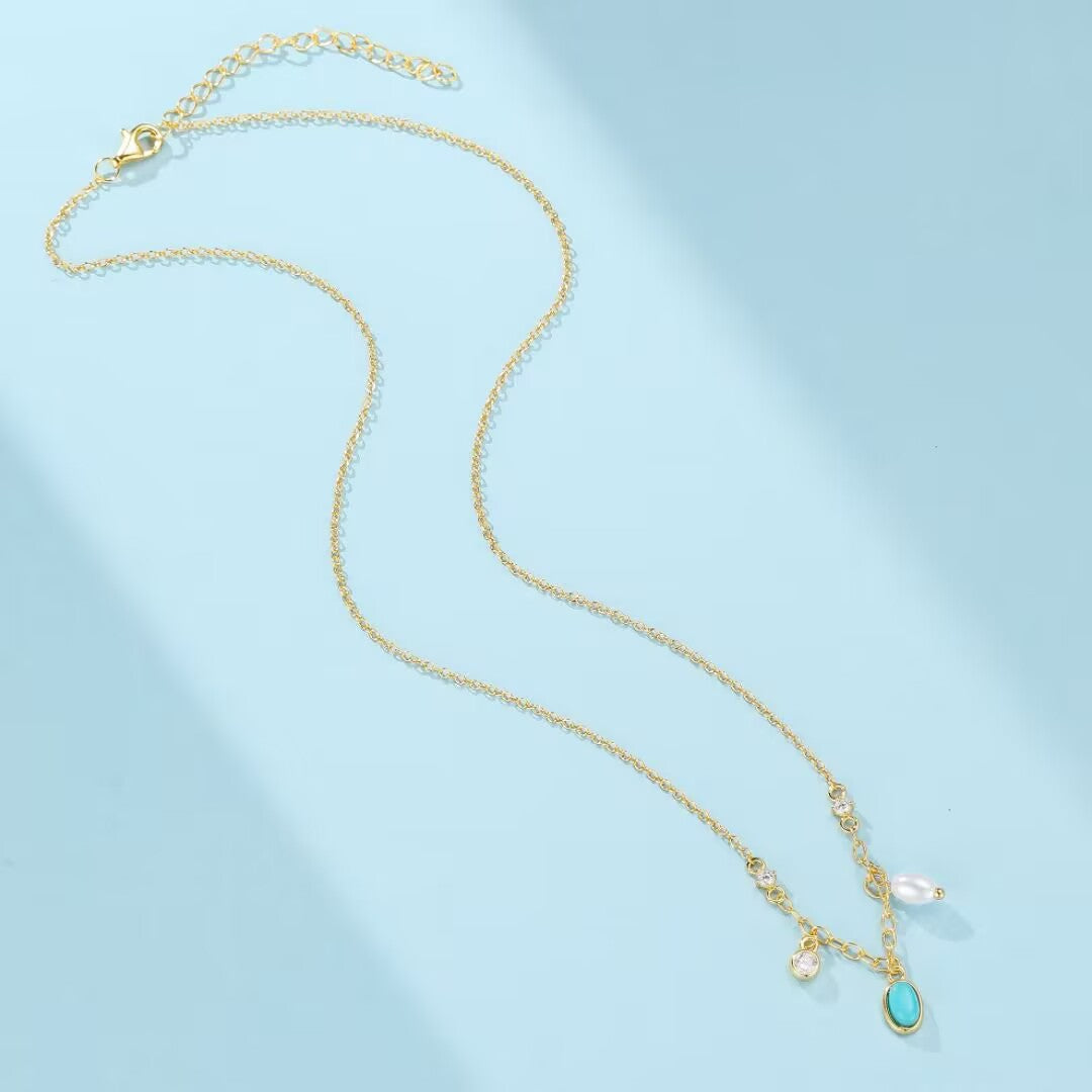 Collier en argent plaqué or avec une turquoise ovale, une perle blanche et des zircons cubiques sur une chaîne délicate.