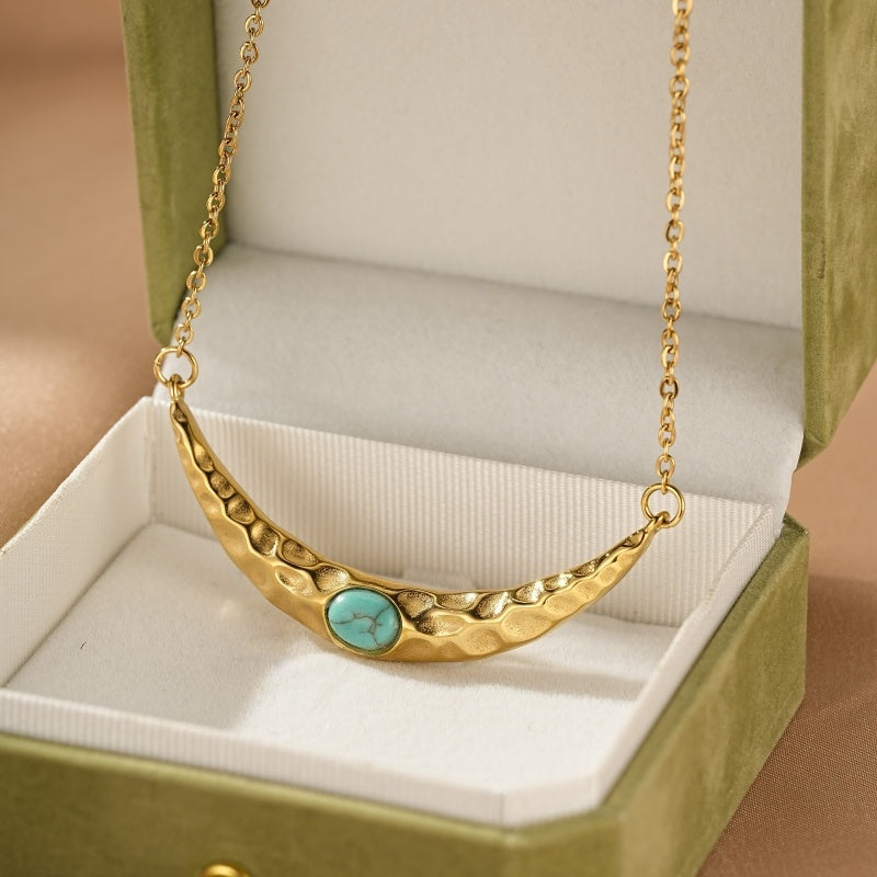 Collier en or avec une pierre turquoise centrale, monté sur une chaîne délicate, présenté dans un écrin vert.