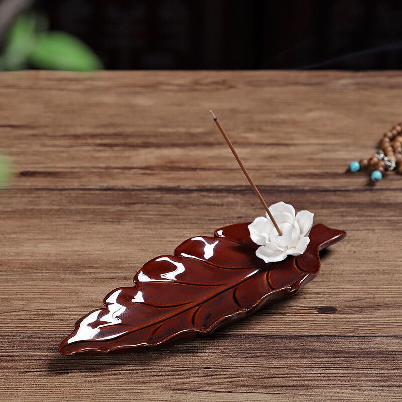 Encensoir en forme de feuille en céramique marron avec une fleur de lotus blanche et un bâton d'encens allumé.