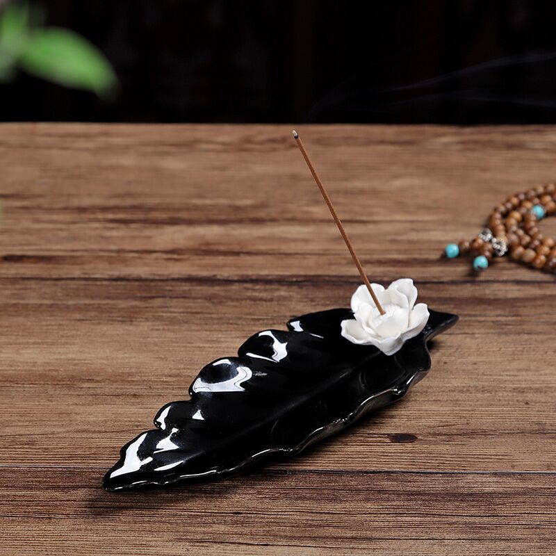 Encensoir en céramique noir en forme de feuille avec une fleur de lotus blanche et un bâton d'encens allumé