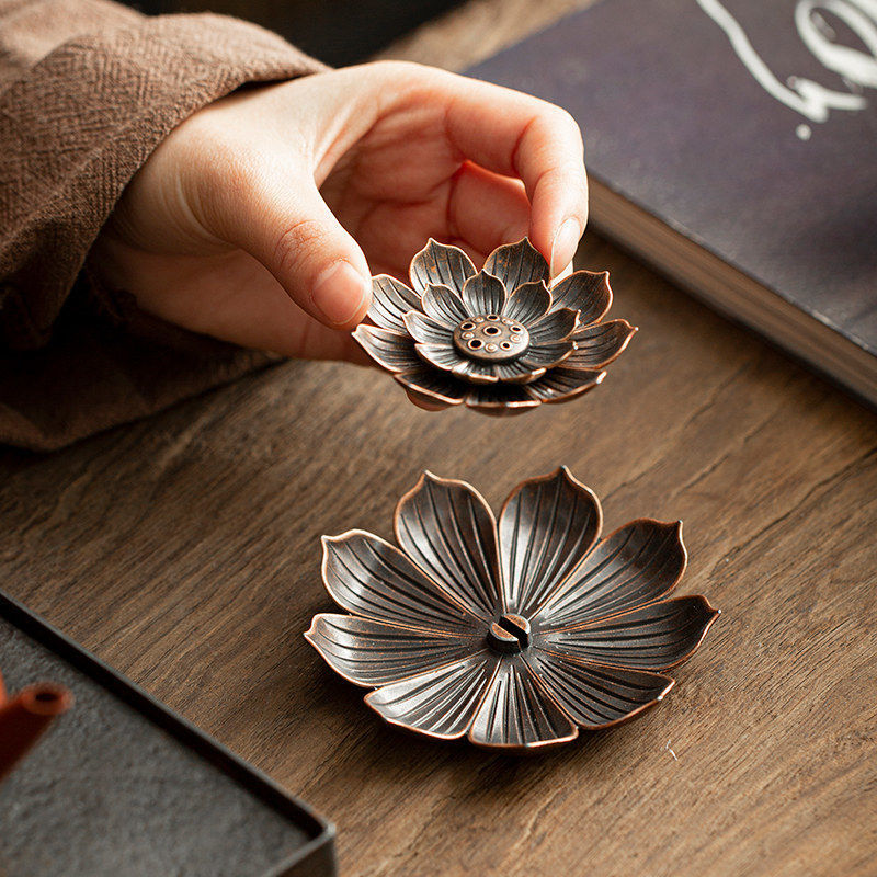 Encensoir en métal en forme de fleur de lotus, tenu par une main, sur un fond en bois.