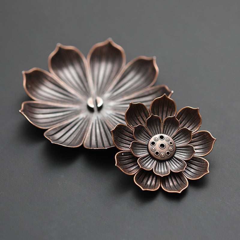 Deux encensoirs en métal en forme de fleur de lotus, l'un plus grand ouvert et l'autre plus petit et fermé, sur fond sombre.