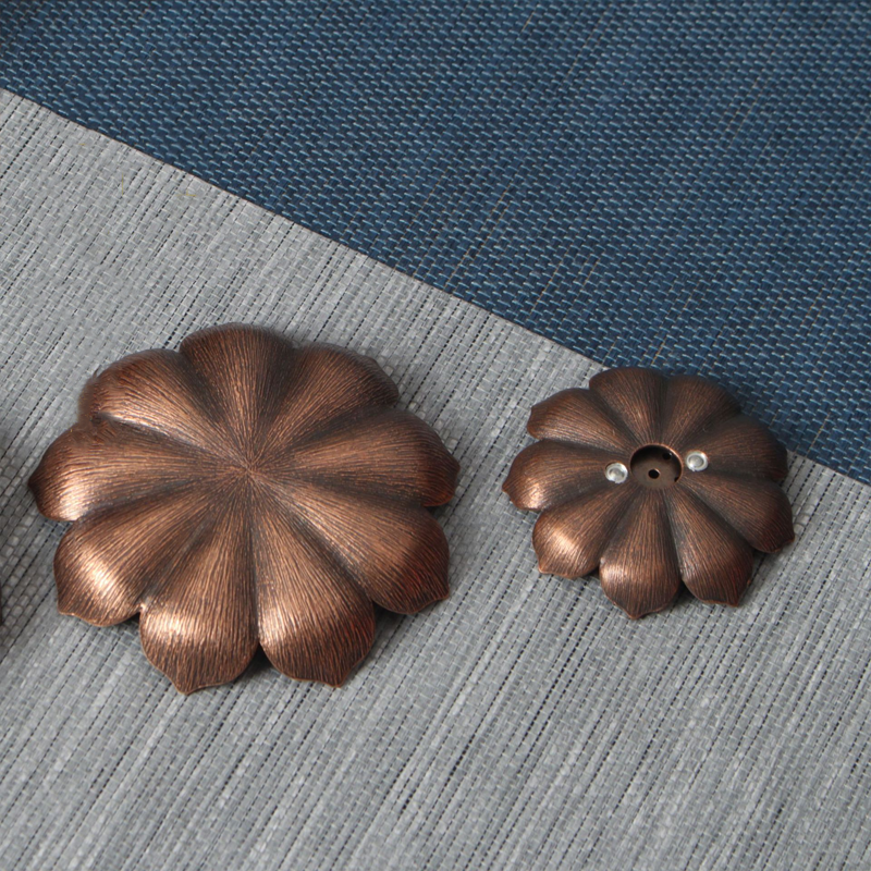 Deux encensoirs en métal de couleur bronze patiné, en forme de fleur de lotus aux pétales stylisés, posés sur un tapis texturé bleu et gris.