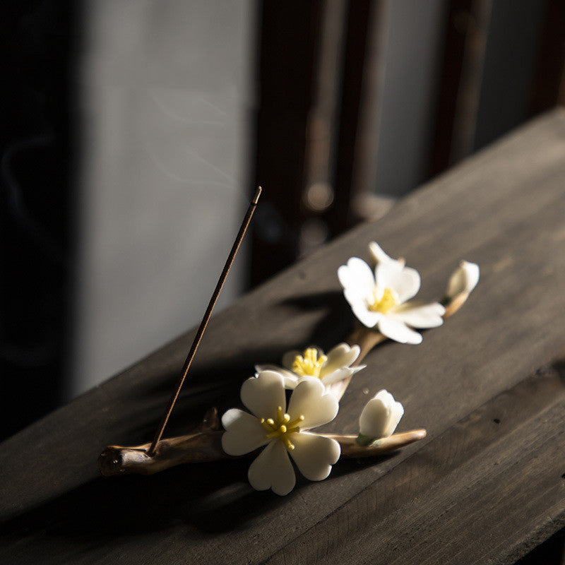 Encensoir zen en céramique fait main en forme de branche fleurie avec une fleur blanche et un bourgeon, une bâton d'encens allumé dégageant de la fumée.