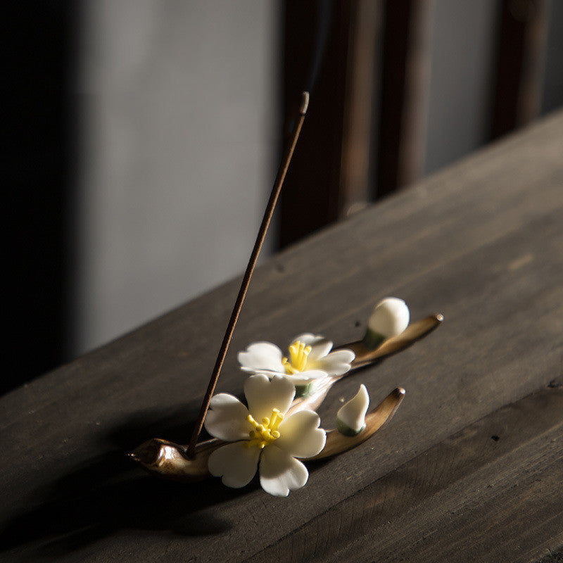 Encensoir Zen en céramique fait main, en forme de branche de cerisier avec des fleurs blanches et un bâton d'encens allumé.