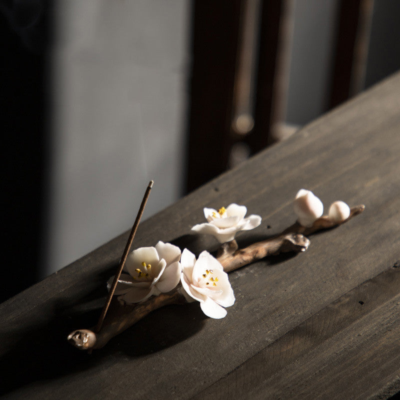 Encensoir zen artisanal en céramique, en forme de branche fleurie de prunier avec des fleurs blanches délicates, supportant un bâton d'encens allumé
