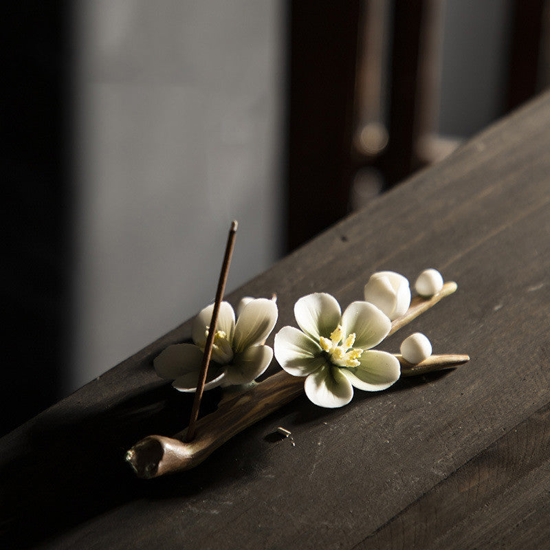 Encensoir zen en céramique fait main, en forme de branche avec des fleurs de cerisier et des perles, tenant un bâton d'encens allumé.