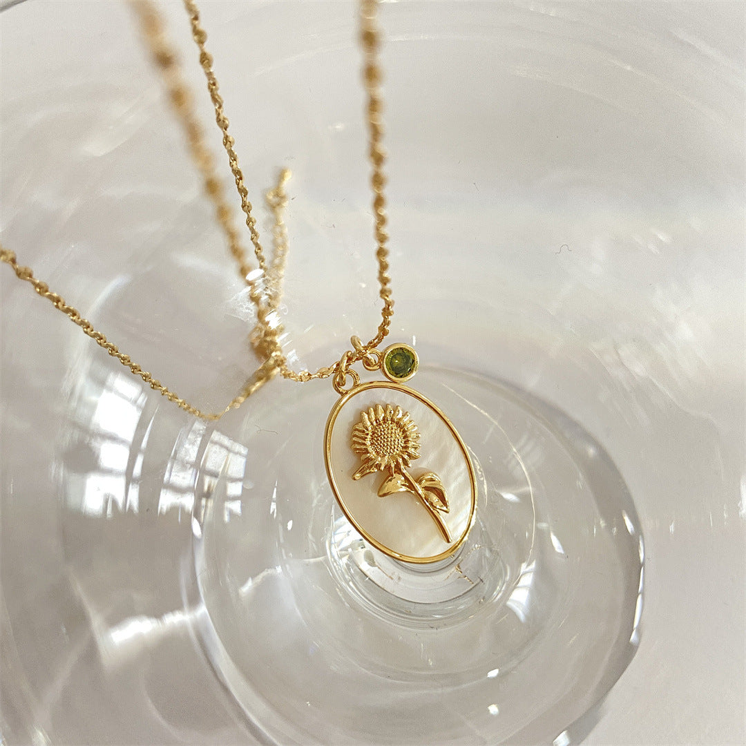 Pendentif Romance en or avec un tournesol sculpté sur une nacre ovale et une petite pierre verte, suspendu à une chaîne délicate.