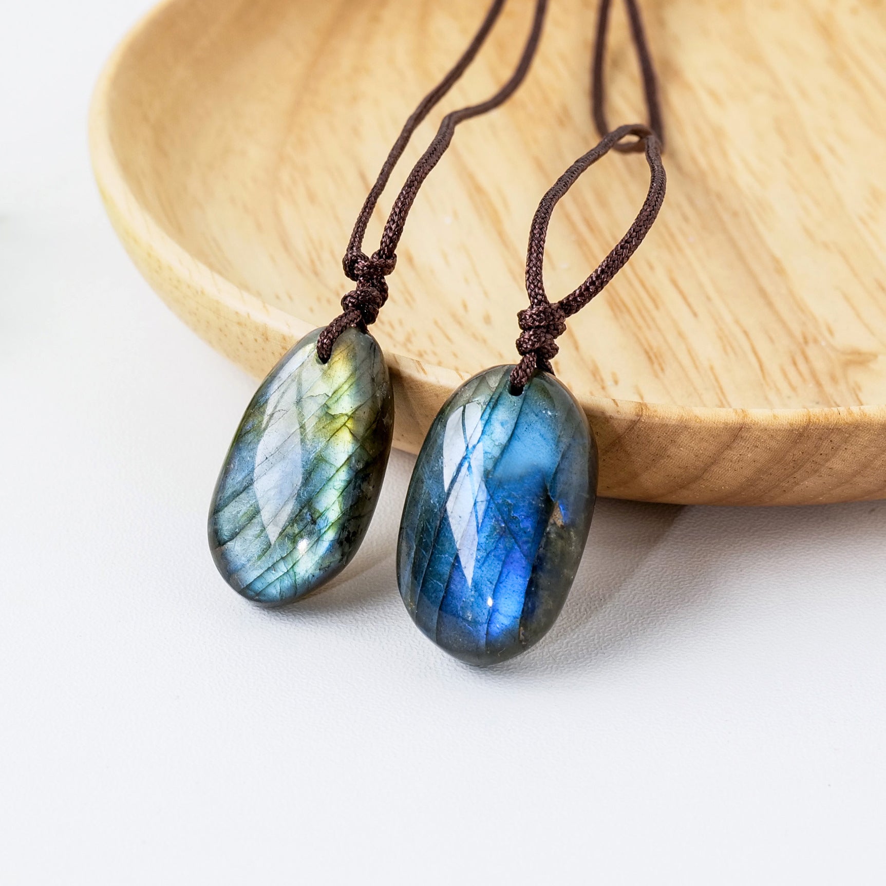 Pendentif en forme d'œuf en pierre de labradorite bleue et verte avec un cordon brun, posé sur un bol en bois.
