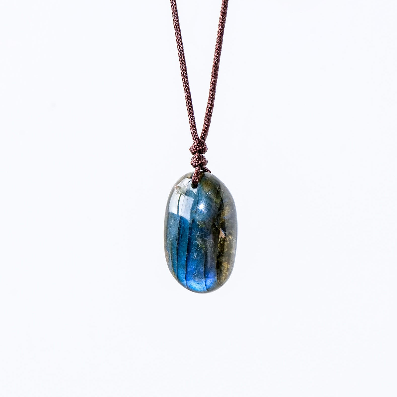 Pendentif ovale en labradorite bleue et verte, suspendu à un cordon marron, sur fond blanc.