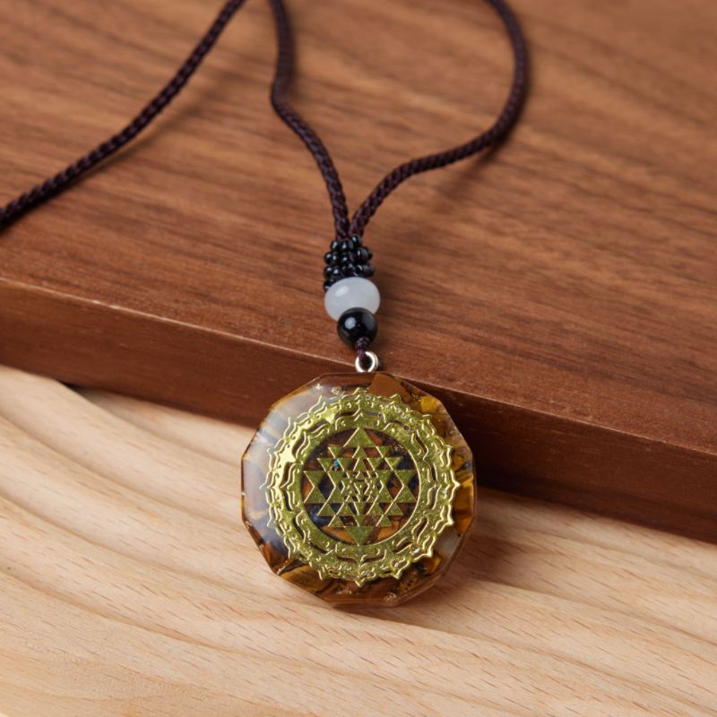 Pendentif Orgonite rond avec symbole Sri Yantra doré et inclusions d'œil de tigre, sur un cordon marron.