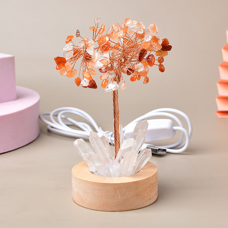 Arbre de vie lumineux en pierres naturelles orange et blanches, avec une base en cristal de roche et un socle en bois, relié par un cùble USB avec interrupteur.