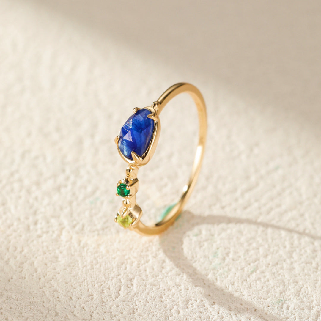 Bague en argent plaqué or sertie d'une aigue-marine bleue en forme de goutte et de petites pierres vertes, dont un péridot.