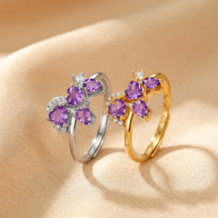 Bague en argent et plaqué or sertie d'améthystes en forme de cœur et de petits cristaux brillants, sur un fond satiné beige.