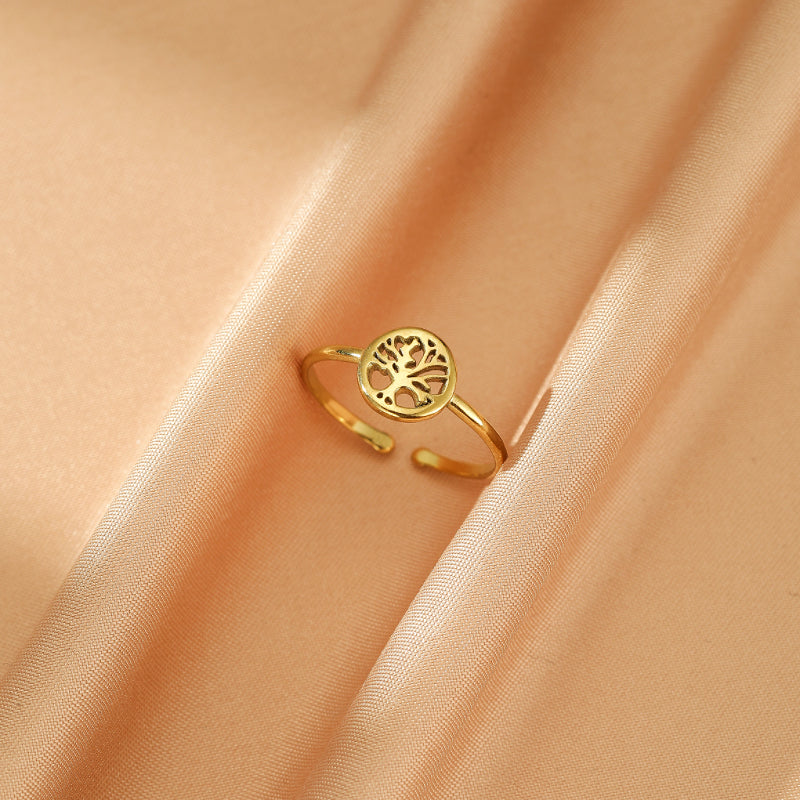 Bague ajustable dorée avec un motif Arbre de Vie ajouré au centre, posée sur un fond satiné de couleur pêche.